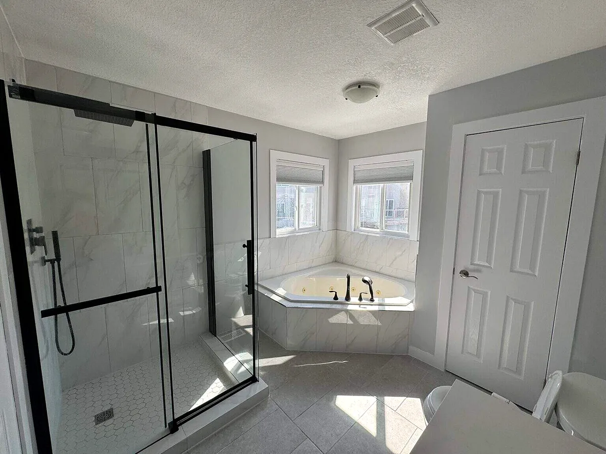 A renovated bathroom with a black-framed glass shower and a corner tub