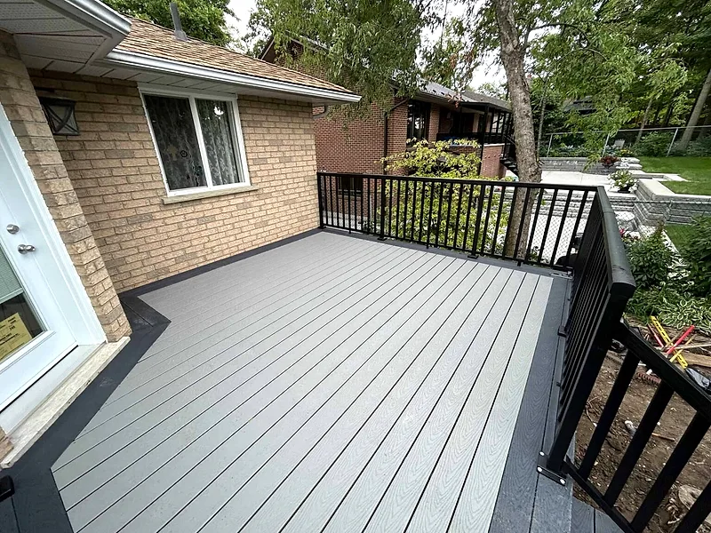A grey composite deck with black metal railings off a brick home