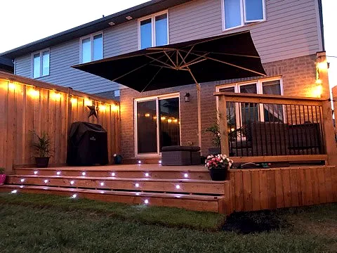 A cedar deck at dusk with string lights and lights set into the steps