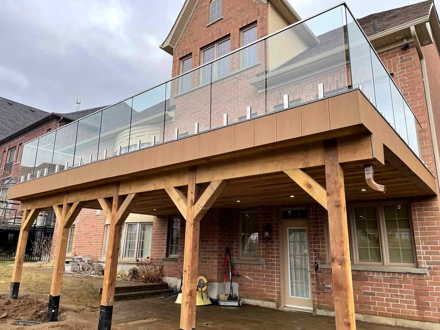 A raised deck with a glass railing on timber posts over a walkout patio