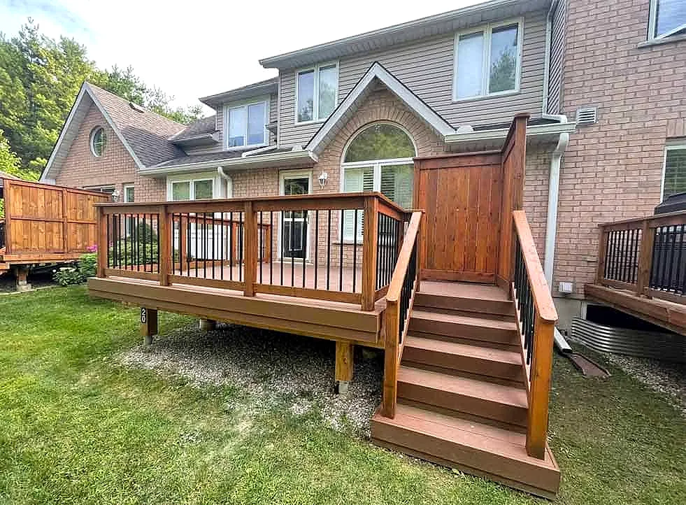 A stained wood deck with a gate and stairs down to the lawn, at the back of a brick home