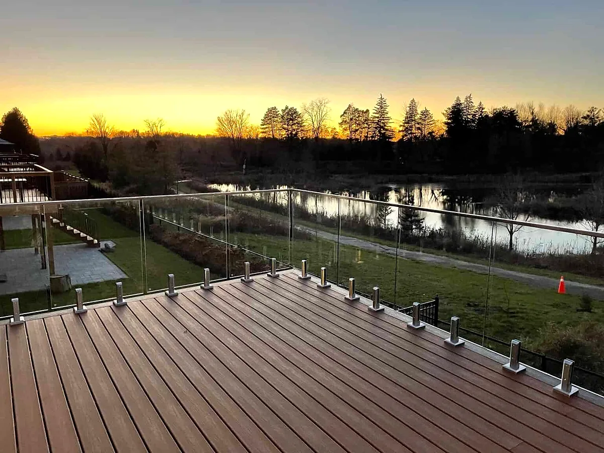A composite deck with a glass railing looking over a pond at sunset