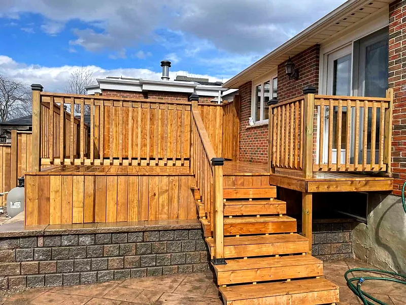 A cedar deck with a landing and wide stairs down to a stone patio